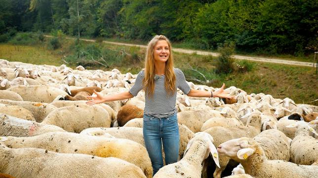 Jana steht inmitten einer Herde von Schafen.