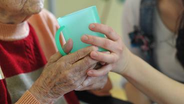 Eine Pflegekraft hilft einer alten Frau beim Trinken aus einem Becher in einem Seniorenheim in Frankfurt (Oder)