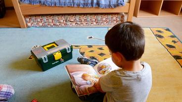 Ein kleiner Junge sitzt auf dem Fußboden und hält ein Kinderbuch in der Hand.