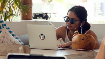 Eine Frau sitzt mit Sonnenbrille vor Ihrem Laptop.