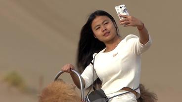 Chinesin auf einem Kamel macht ein Selfie