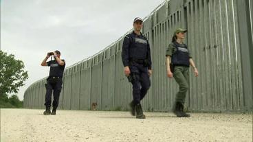 Zwei Polizisten und eine Polizistin patroullieren am Grenzzaun