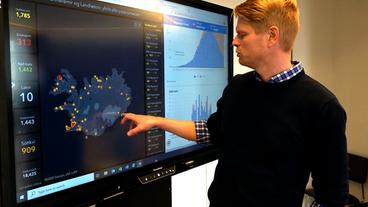 Auf einem Bildschirm zeigt ein Mann verschiedenfarbige Punkte über Island verteilt.