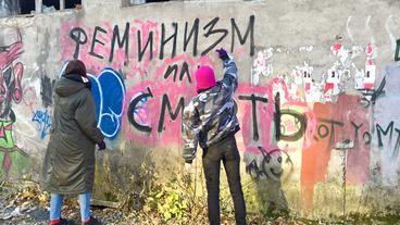 Zwei Frauen sprühen Graffiti an eine Wand.