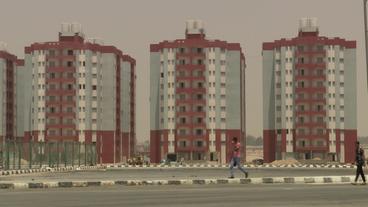 Drei fast identische Hochhäuser, davor eine Straße im Bau befindlich, zwei Menschen gehen darauf  