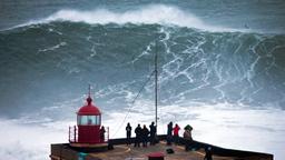 Personen schauen einem Surfer zu, der vor Nazar auf einer riesigen Welle reitet.