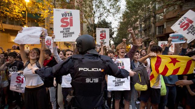 Kalanische Demonstranten fordern auf Schildern die Unabhängigkeit Kataloniens von Spanien und ein Polizist versucht sie zurückzuhalten.