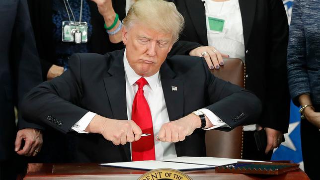 Donald Trump nimmt einen Stift um ein Dekret zu unterschreiben.