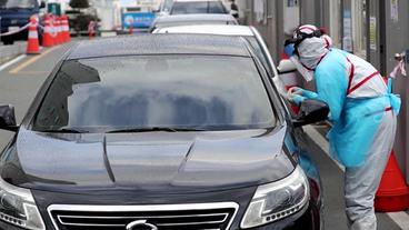 Eine Person im Schutzanzug reicht ein Mundstäbchen in ein Auto.
