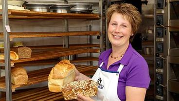 Irmgard nimmt lächelnd ein frisches Brot aus dem Regal