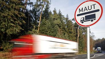 Lastkraftwagen fahren an einem Straenschild mit dem Hinweis zur Lkw-Maut vorbei.