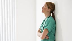 Eine Pflegekraft lehnt mit geschlossenen Augen an einer Wand