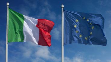 Ein italienische und eine EU-Flagge wehen im Wind an zwei Fahnenmasten.