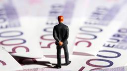 Ein Spielzeugmnnchen steht vor Banknoten