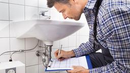 Handwerker kniet vor einem Waschbecken und macht sich Notizen