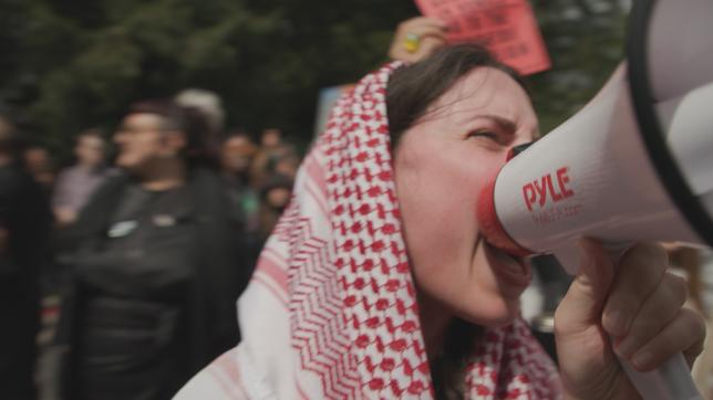 Eine Frau mit Palästinensertuch ruft in ein Megafon