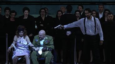 Theaterbühne: Ein Mann richtet eine Pistole auf ein gefesseltes Paar