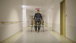 Thomas Binder mit dem Exoskelett gehend, auf Krcken gesttzt, im Krankenhausflur.