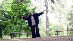 Alte Frau steht im Park auf einem Bein.
