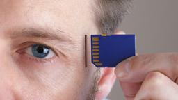 Ein Mann steckt eine SD-Card in den SD-Card-Slot an seiner Schlfe.