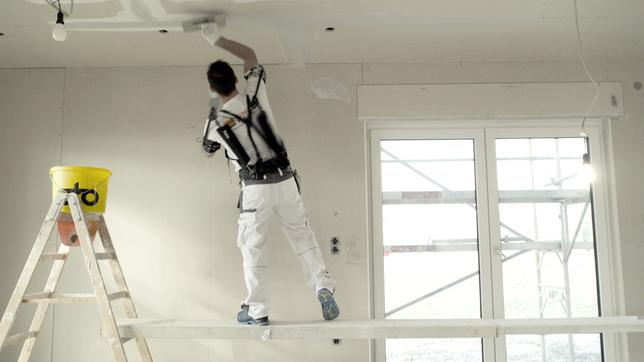 Maler mit Exoskelett auf einer Baustelle.