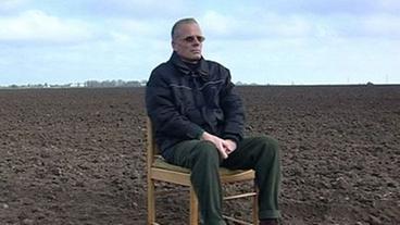 Mann sitzt im Regiestuhgl auf einem Feld