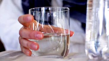 Eine Hand greift nach einem Wasserglas
