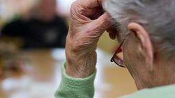 Eine ltere Frau sttzt ihren Kopf auf die Hand. Es ist nur der Hinterkopf und die Brille zu sehen.