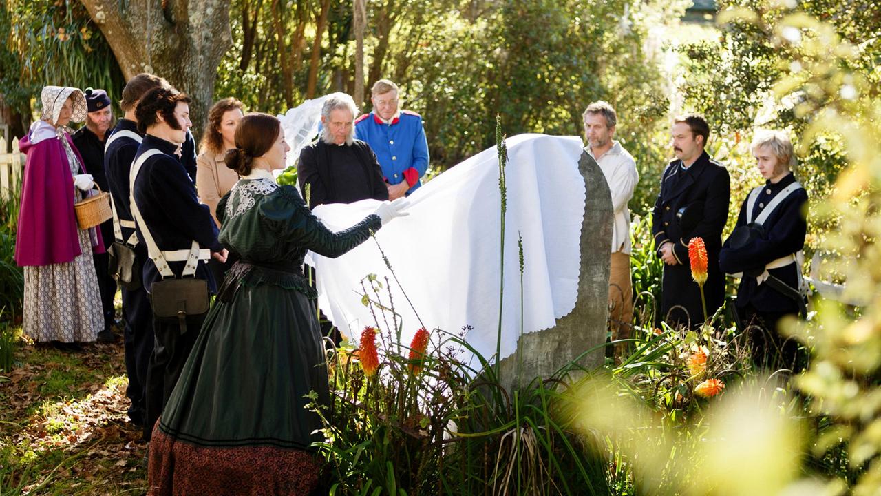 Charity (Jacqueline Nairn, vorne) enthüllt mit den Bewohnern des viktorianischen Museumsdorfes einen Grabstein.