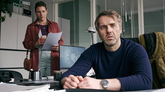 Jochen Mohn (Stefan Rudolf) sitzt gedankenverloren an seinem Schreibtisch. Hinten: Kriminalhauptkommissarin Hermine Grill (Xenia Tilling).