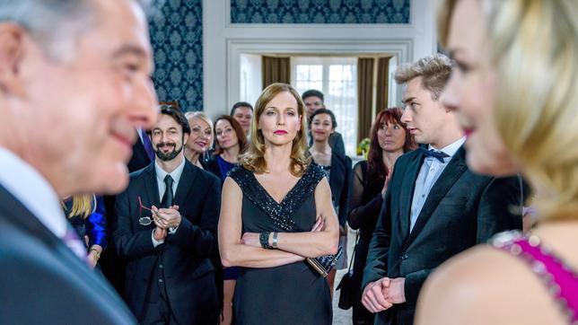 André (Joachim Lätsch) stellt Nina (Saskia Valencia) als die neue Frau an seiner Seite vor. Chris (Beate Maes) und Norman (Niklas Löffler, 2.v.r. mit Komparsen) sind davon wenig begeistert.