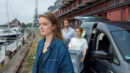 Emily (Hannah Dalmeyer) blickt melancholisch auf das Boot ihrer verstorbenen Freundin. Im Hintergrund laden Marold (Dominik Maringer) und Viktoria (Wanda Perdelwitz) Kisten aus dem Auto.