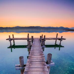 Holzsteg am Pfaeffikersee im Gegenlicht bei Sonnenaufgang mit Blick zum Bachtel und Glaernisch im Hintergrund, Schweiz, Pfaeffikon