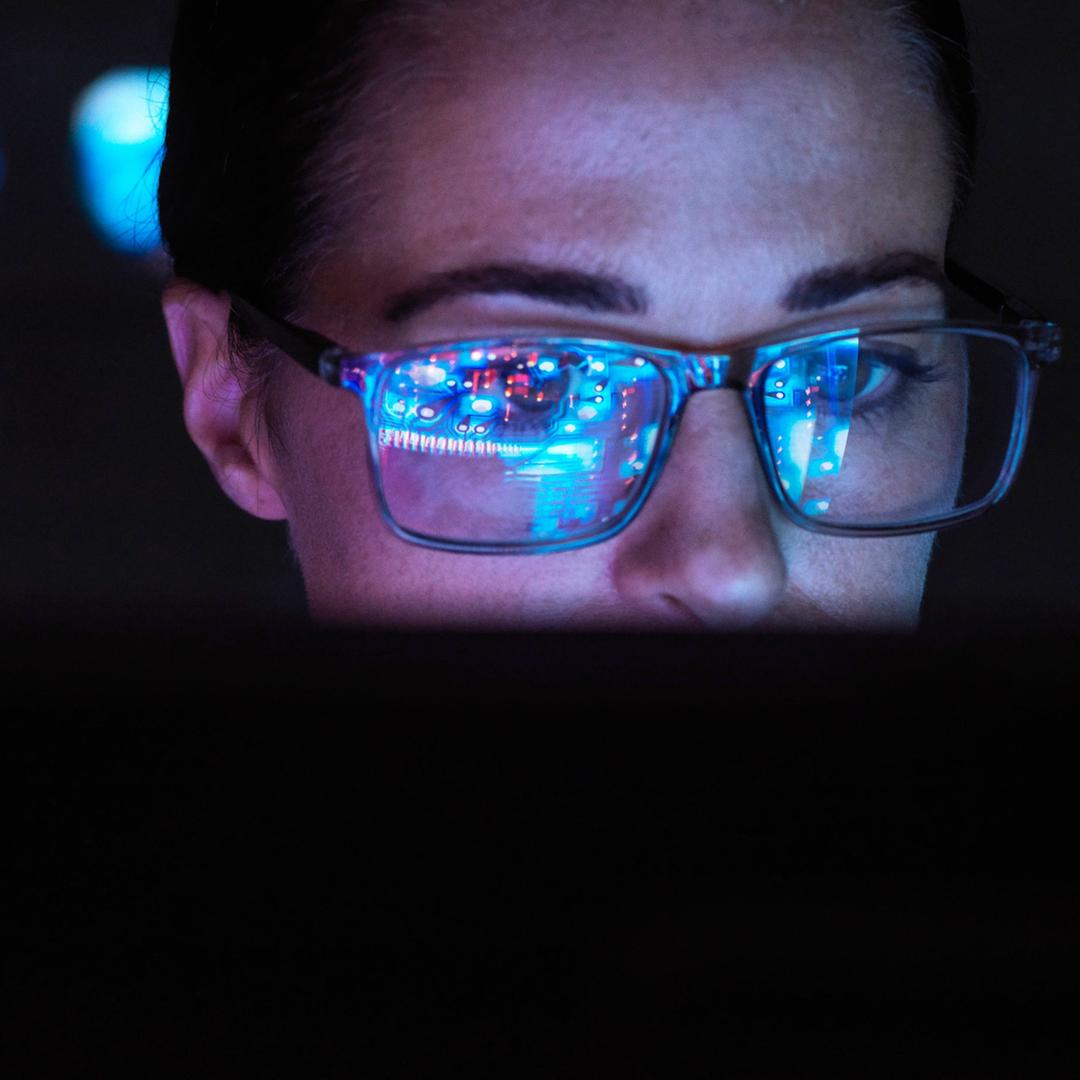 In der Brille einer Frau spiegelt sich ein Bildschirm.