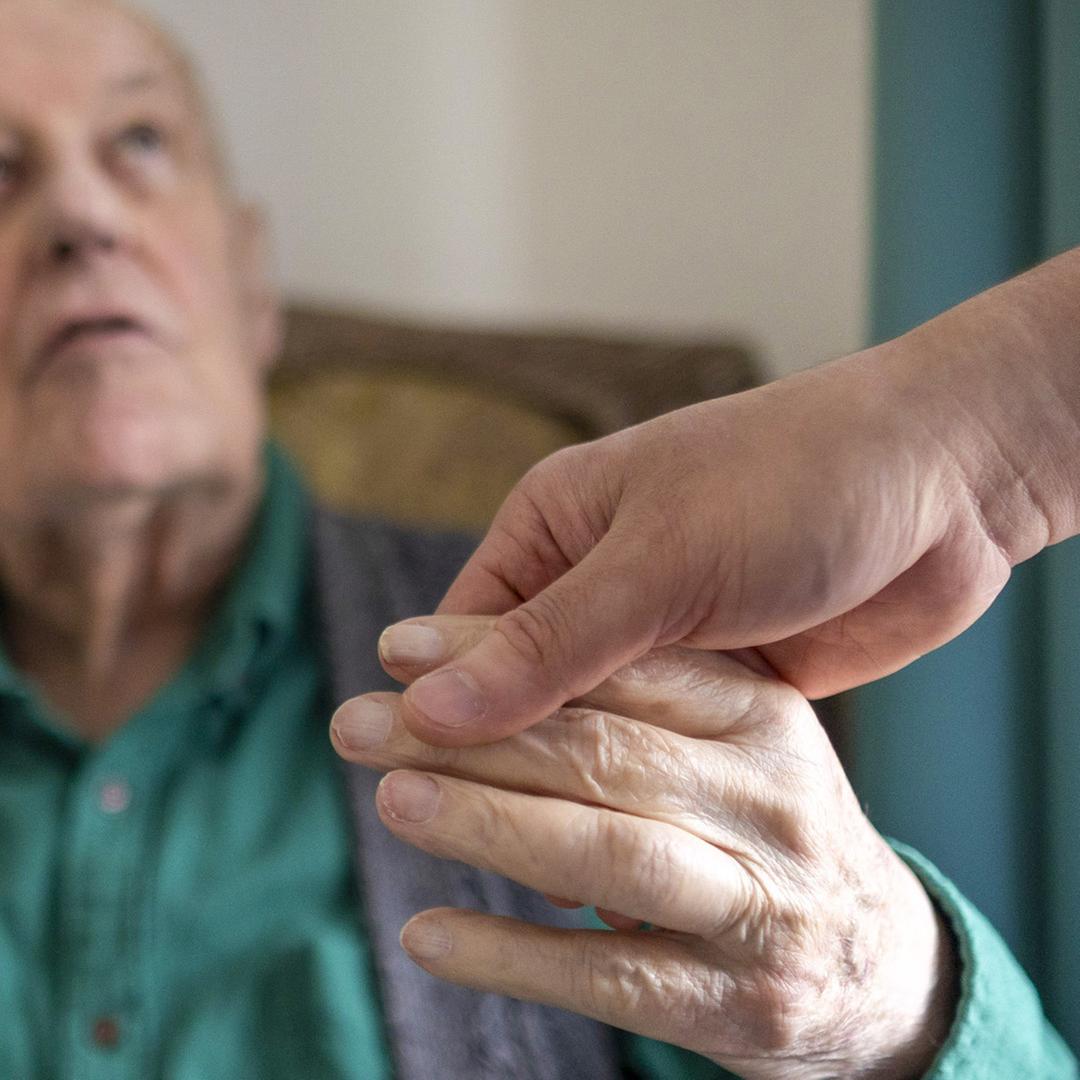 Altenpfleger haelt die Hand eines alten Mannes im Pflegeheim 