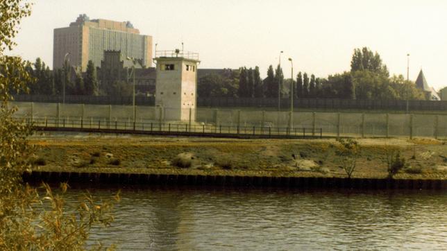 Die Charité liegt während der deutschen Teilung im Osten, in der DDR. Das berühmteste Krankenhaus Deutschlands im Spannungsfeld des Kalten Krieges. Ein Ort der Lehre, Forschung und Heilung – und das beste Krankenhaus im Ostblock. Doch Anfang der 60er Jahre blutet die Charité fast aus: Immer mehr Ärzte gehen in den Westen. Bis zum 13. August 1961. Fortan liegt das Krankenhaus im Mauerschatten. - Wachturm Mauer vor der Charité in Berlin Mitte von Westberlin aus.