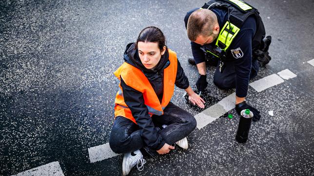 Ein Polizist löst die angeklebte Hand einer Aktivistin bei einer Straßenblockade der "letzten Generation" auf dem Kurfürstendamm in Berlin.
