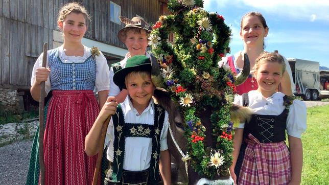 In den Ferien helfen Kinder aus der Nähe auf der Alpe. Hannes (vorne links), Magdalena (vorne rechts) und Jona (Mitte hinten) und zwei Helferinnen stehen neben der geschmückten Kuh „Lena“.