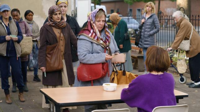 Tina steht für die Markenausgabe bei der Tafel an. Hinter ihr wartet auch Fatma, deren Berechtigungsschein mal wieder nicht gültig ist.