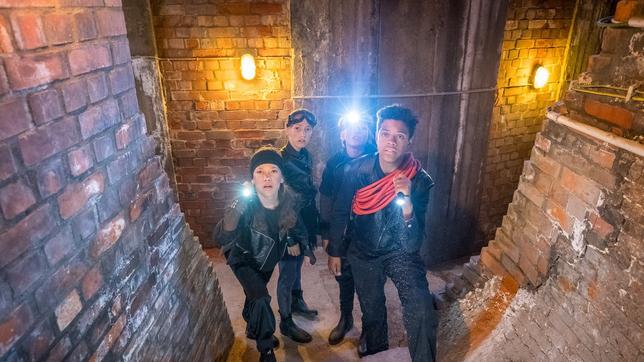 Kira, Nele, Levin und Tayo sind mit Taschenlampen in einem Kellergewölbe unterwegs