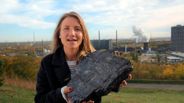 Bild: WDR Jana steht auf einem Hügel vor der Kokerei Prosper im Ruhrgebiet. Sie hält ein großes Stück Steinkohle in der Hand.
