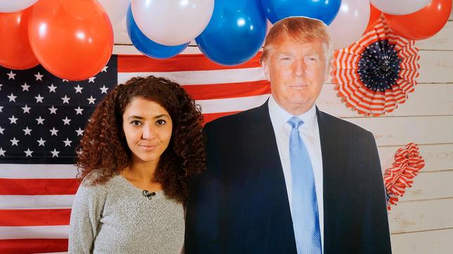 Moderatorin Siham mit einem Pappaufsteller von Donald Trump.