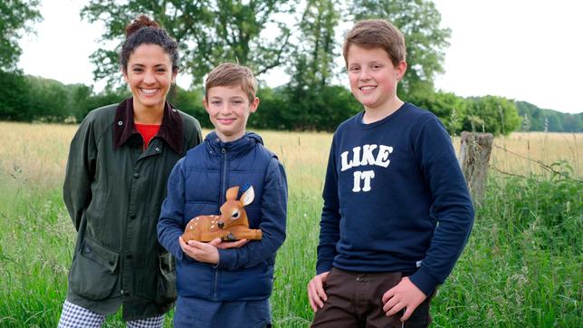 Siham mit den Rehkitzrettern Henk und Marlon auf einem Feld bei Halle (Westfalen). Henk hält eine Rehkitz-Figur im Arm.