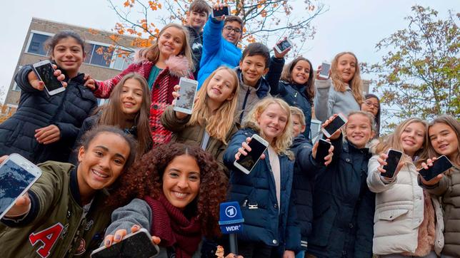 Siham mit Sechstklässlern des Mataré-Gymnasiums in Düsseldorf, alle präsentieren ihre Smartphones.