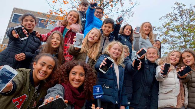 Bild: WDR/tvision Siham mit Sechstklässlern des Mataré-Gymnasiums in Düsseldorf, alle präsentieren ihre Smartphones.