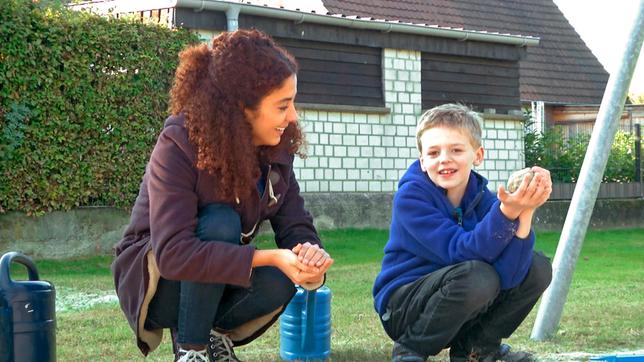 Siham und Timo spielen in Timos Garten mit Sand.