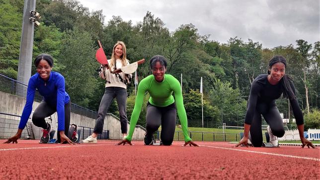 Die Drillinge Dörte, Dorina und Dorinda in Startposition auf dem Sportplatz. Hinter ihnen schlägt Jana die Start-Klappe.