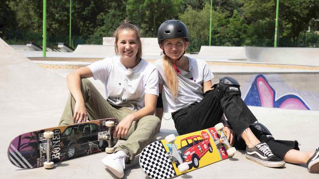 Jana und Lea sitzen mit ihren Skateboards auf einer Skateboard-Rampe.