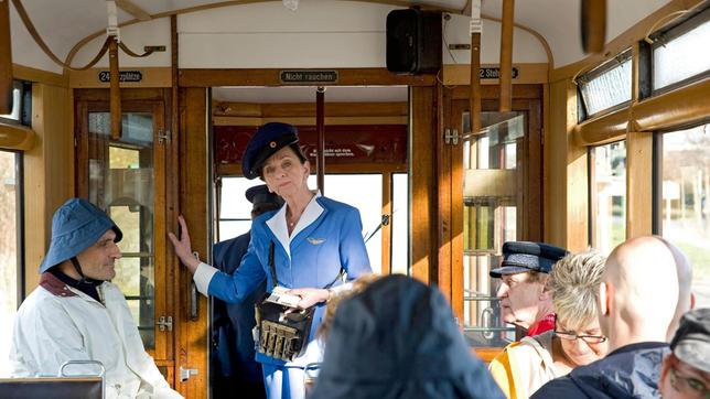 Bild: MDR/Katharina Simmet Direktor Berger (Robert Schupp) bemerkt verdutzt, dass Frau Rottbach (Angelika Böttiger) in der Tram als Schafferin arbeitet.