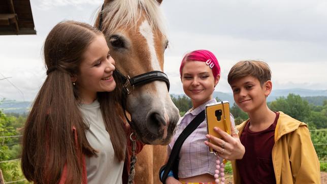 Lucy (Paulina Schnurrer, links) und Liam (Nils Hofschneider, rechts) sind superglücklich. Ihre Lieblings-Influencerin Tara Lovely (Carlotta Truman, Mitte) ist zu Besuch in Waldau.